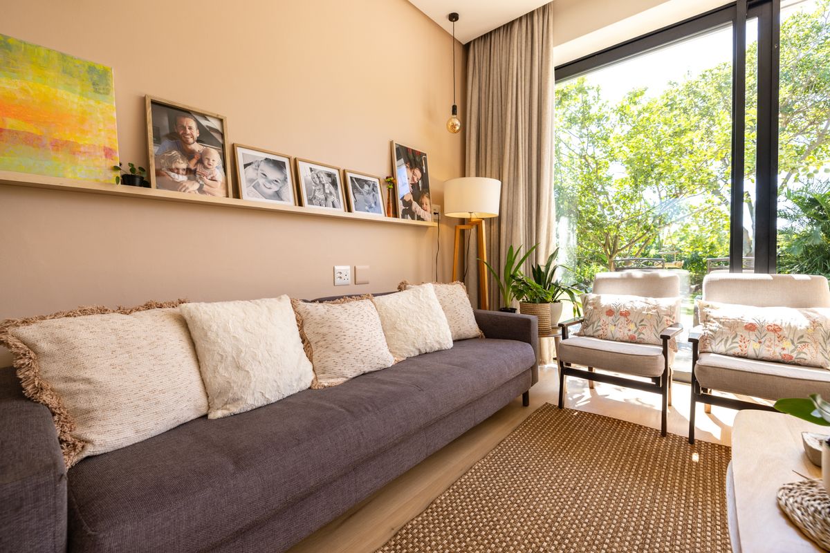 A bright living room featuring large floor-to-ceiling windows with garden views, neutral wall tones, and modern light wood flooring.
