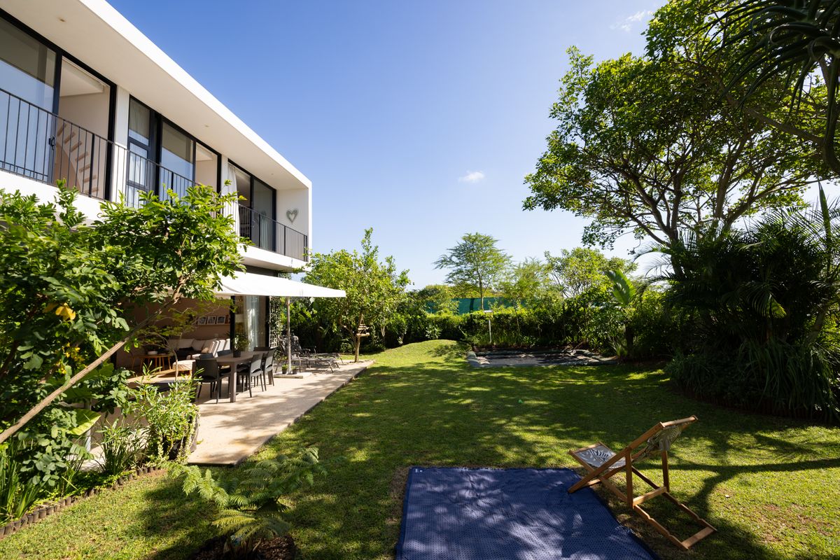A spacious rear garden featuring a paved patio area, lush lawn, mature trees, and direct access to the modern two-story residence.