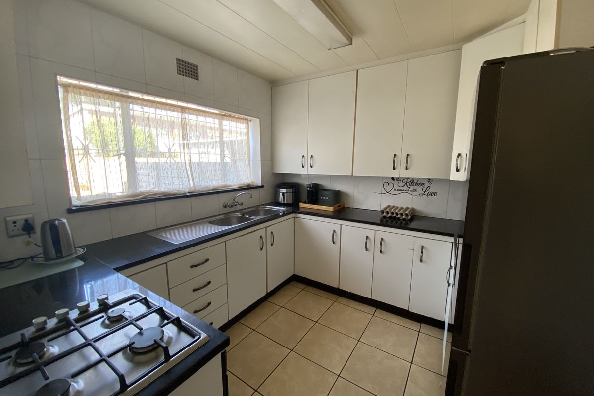 A functional kitchen featuring white cabinetry, dark countertops, a built-in gas hob, and tiled flooring with a large window for natural light.