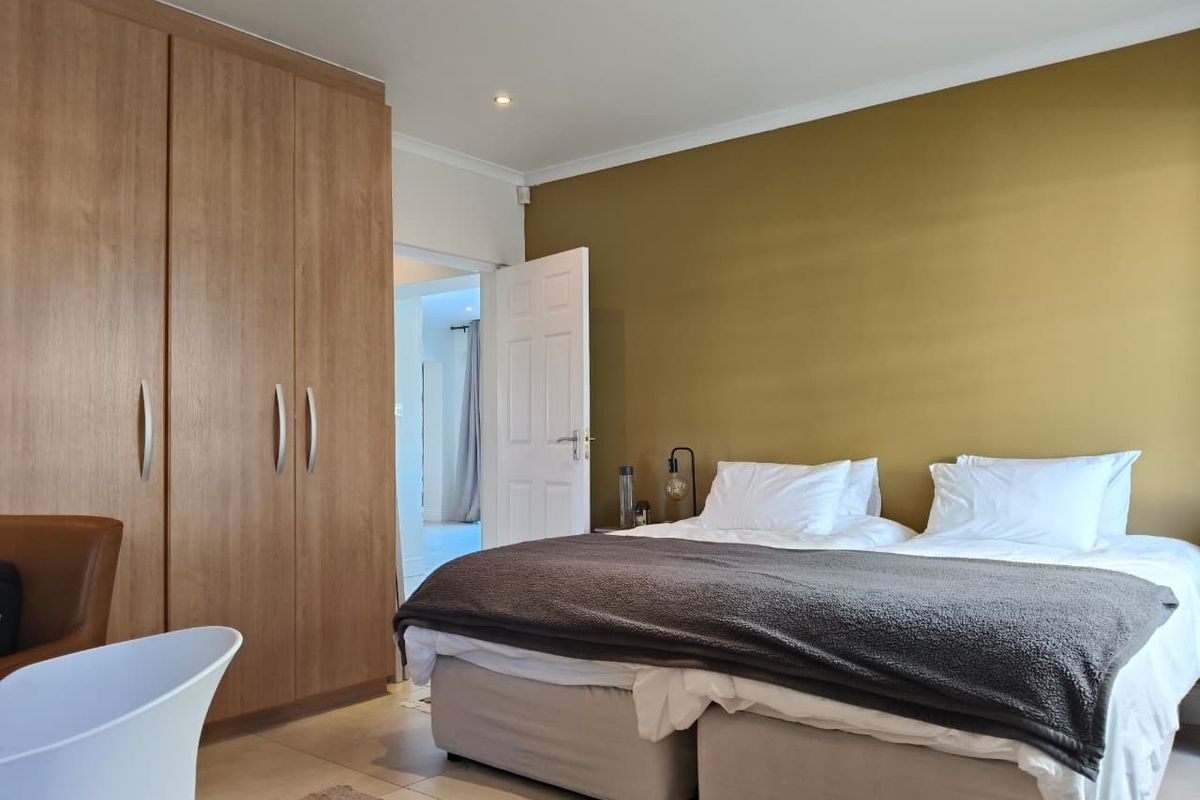 A well-maintained bedroom featuring built-in wooden wardrobes, tiled flooring, and a feature wall, with an adjoining doorway leading to another room.