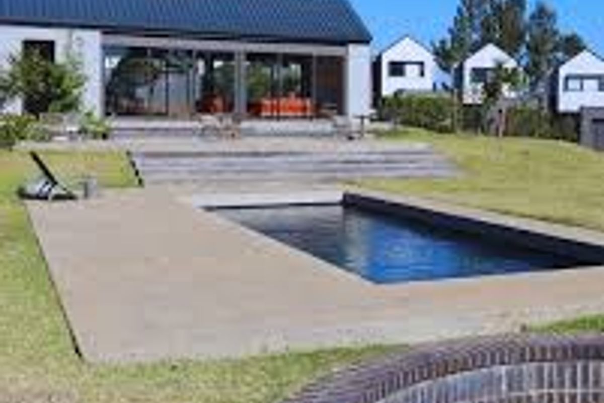Rear view of the townhouse featuring a swimming pool, paved patio area, and a sunken fire pit set within a landscaped garden.