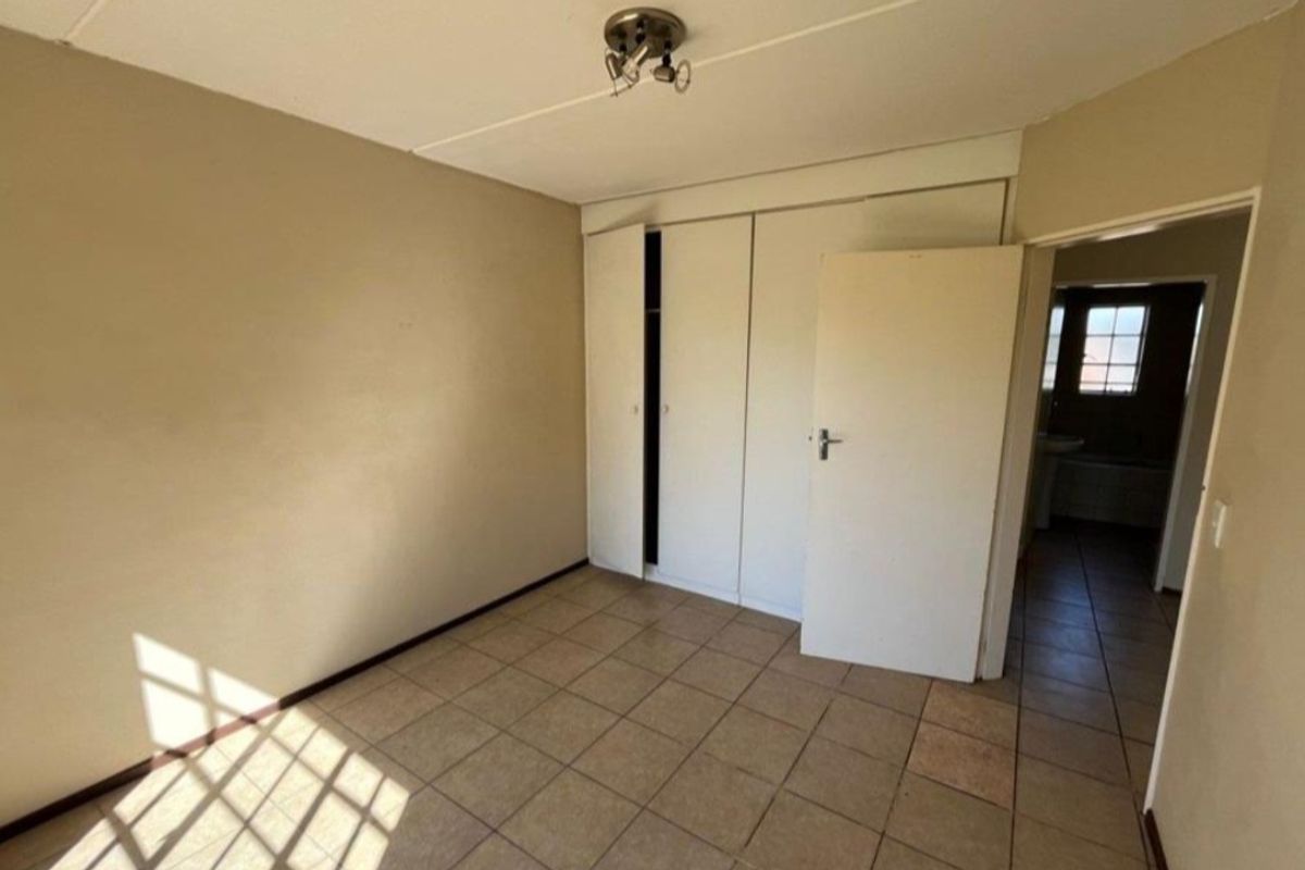 A vacant bedroom featuring built-in cupboards, tiled flooring, and direct access to an adjacent bathroom area.