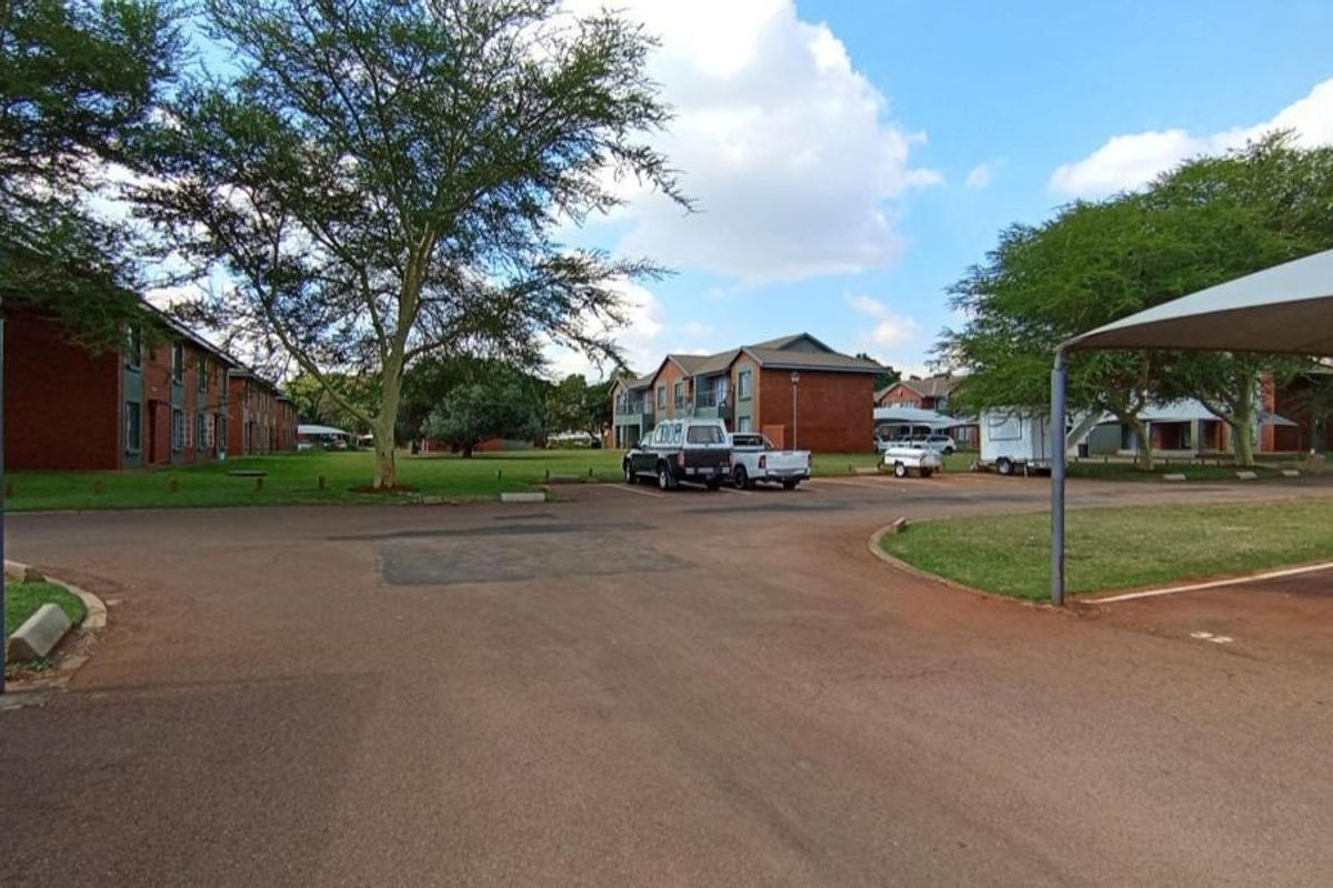 Exterior view of the apartment complex grounds featuring paved parking areas, shade-cloth carports, and established green lawns between residential buildings.