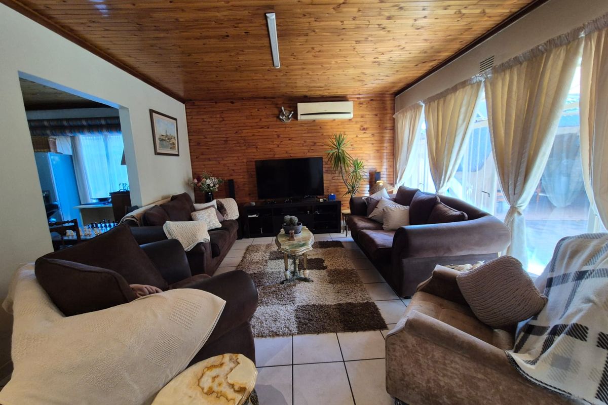 A spacious living room featuring tiled flooring, timber-paneled walls and ceiling, and a wall-mounted air conditioning unit.