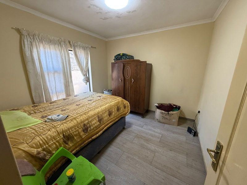 A bedroom featuring wood-look tile flooring and a window with curtain tracks. The ceiling shows visible signs of water damage.