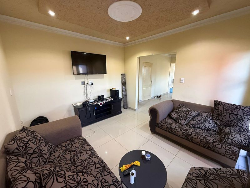 A living room featuring tiled flooring, recessed ceiling lighting with a decorative medallion, and a wall-mounted television setup.