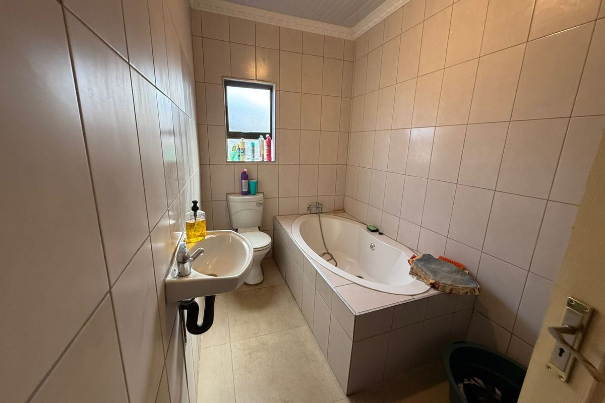 A functional bathroom featuring a built-in bathtub, wall-mounted basin, and toilet, finished with neutral wall and floor tiling.