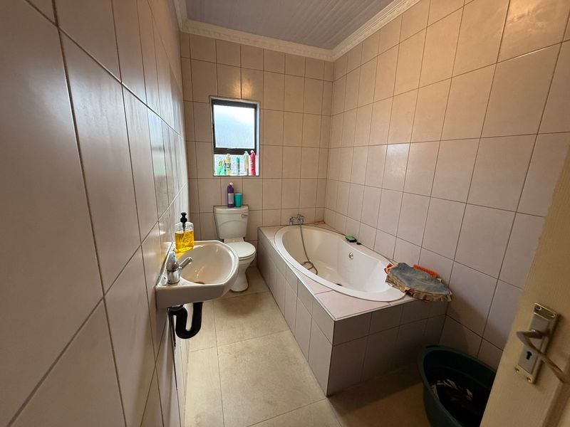 A functional bathroom featuring a built-in bathtub, wall-mounted basin, and toilet, finished with neutral wall and floor tiling.