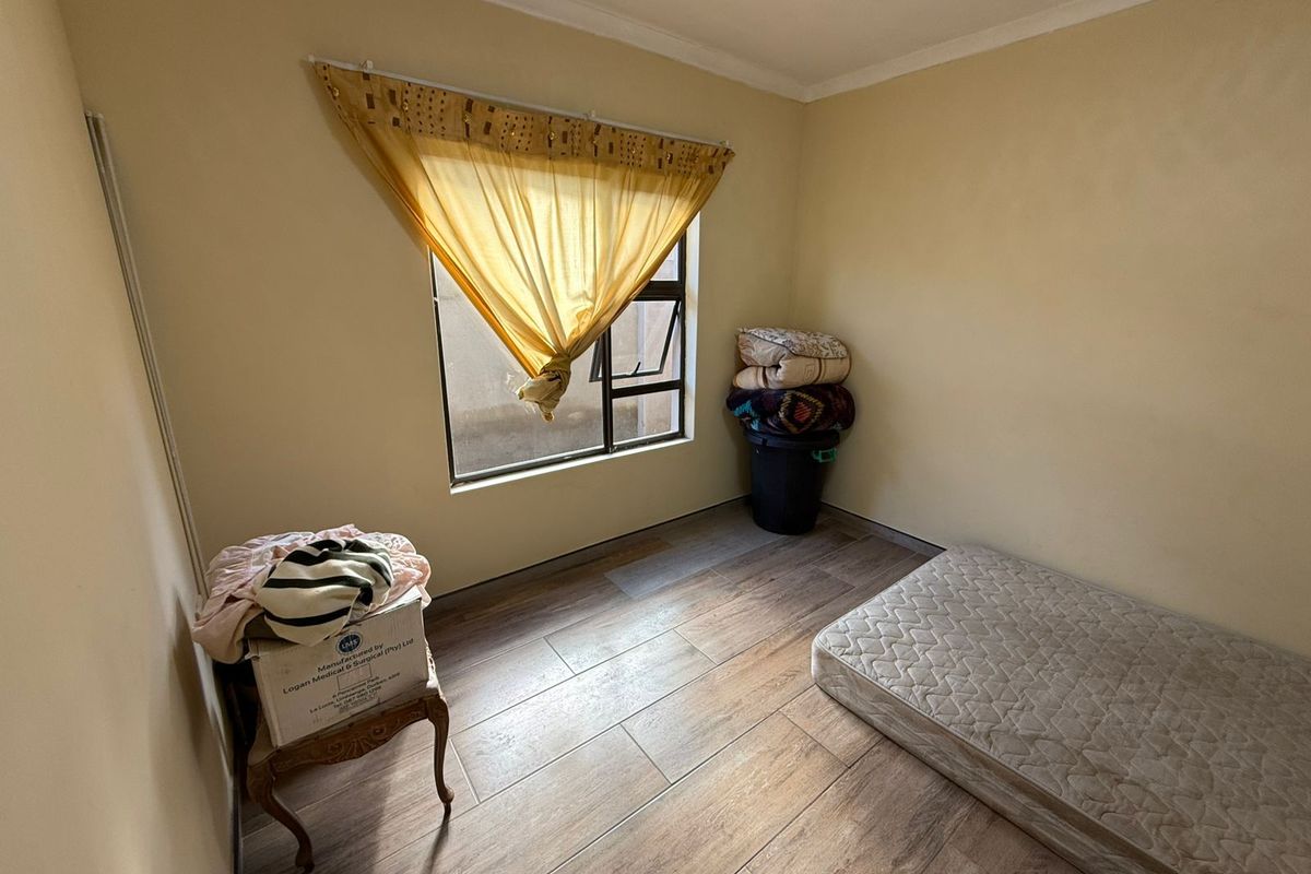 A compact bedroom featuring wood-look tiled flooring and a single window, offering a functional space ready for renovation or staging.