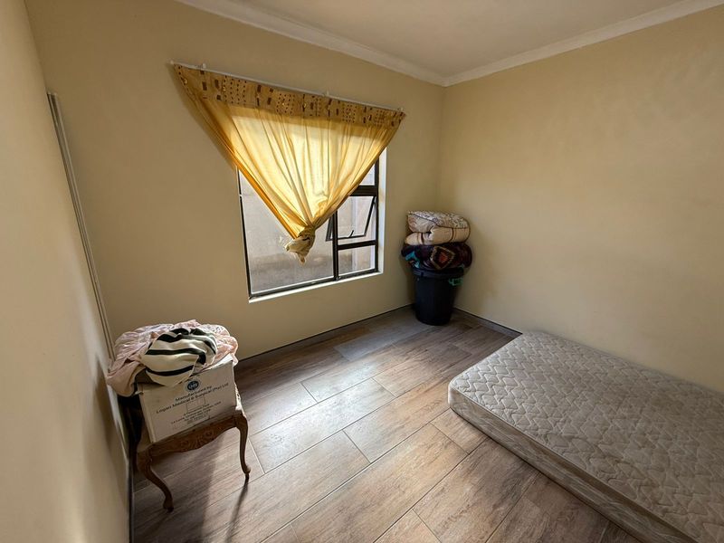 A compact bedroom featuring wood-look tiled flooring and a single window, offering a functional space ready for renovation or staging.