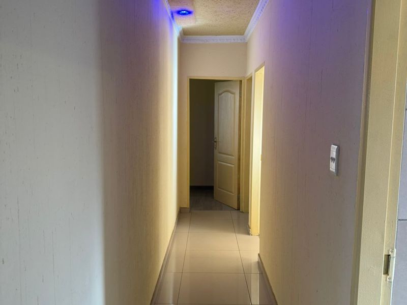A narrow hallway featuring tiled flooring, recessed blue accent lighting, and multiple doorways leading to adjacent rooms.