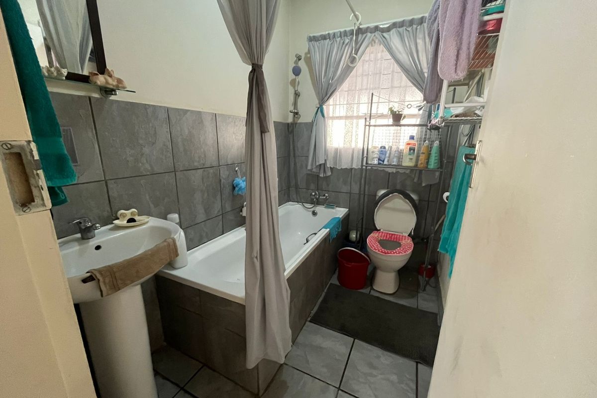 A functional bathroom featuring a pedestal basin, bathtub with shower mixer, and toilet, finished with grey wall and floor tiling.