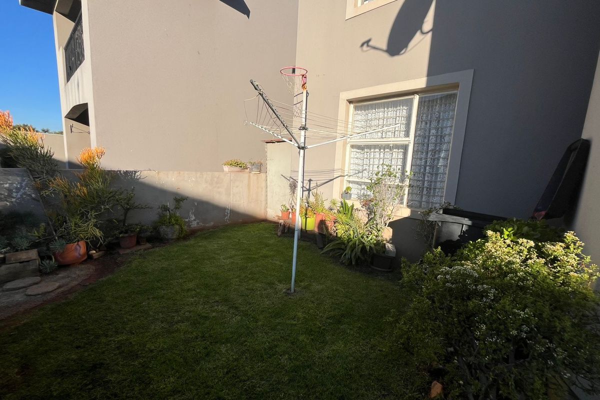 A private rear garden area featuring a small lawn, perimeter boundary wall, and exterior building facade with window access.