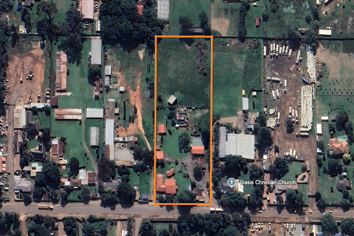 Aerial view of a small holding property featuring multiple structures, open land, and established trees within a defined boundary.