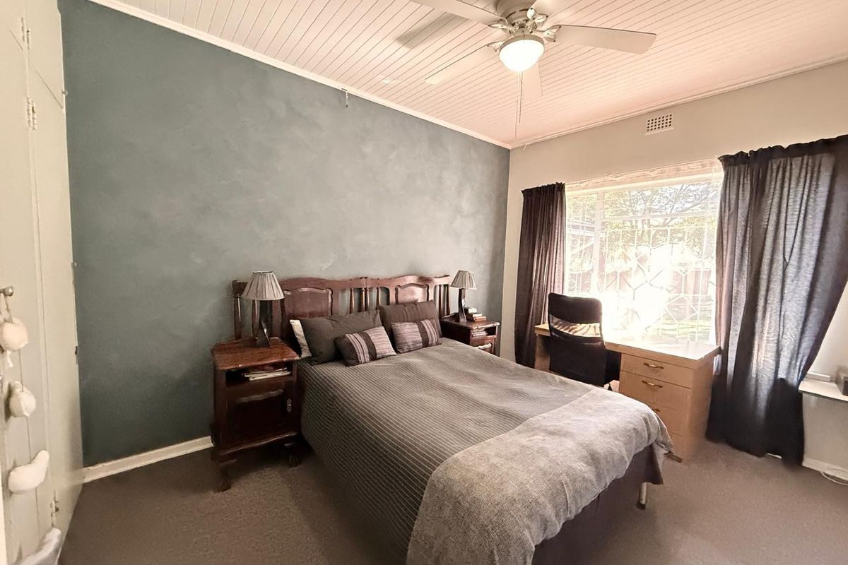 A bedroom featuring a textured accent wall, built-in cupboards, a ceiling fan, and a window with security bars.