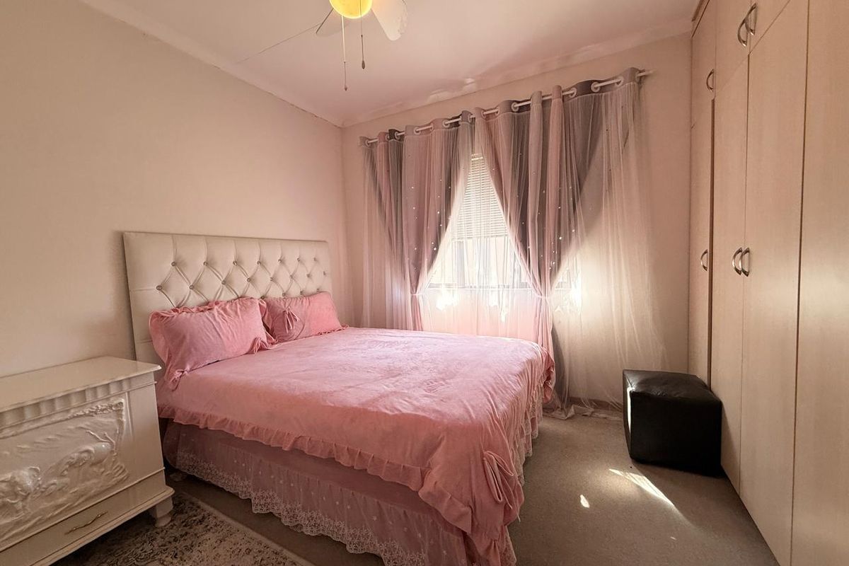 A cozy bedroom featuring built-in floor-to-ceiling wardrobes, a ceiling fan, and natural light filtering through window treatments.