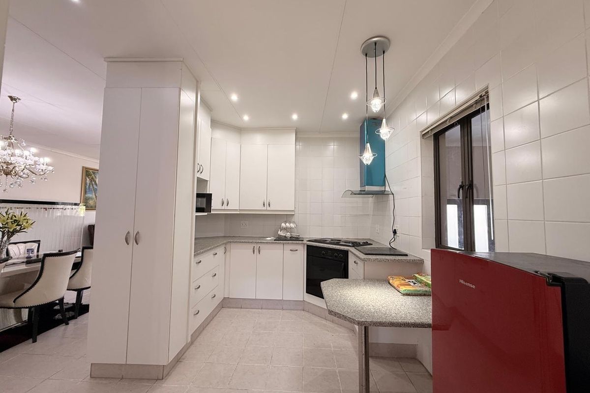 A functional kitchen featuring white cabinetry, granite countertops, a built-in oven, hob, and extractor fan, with tiled flooring and recessed lighting.