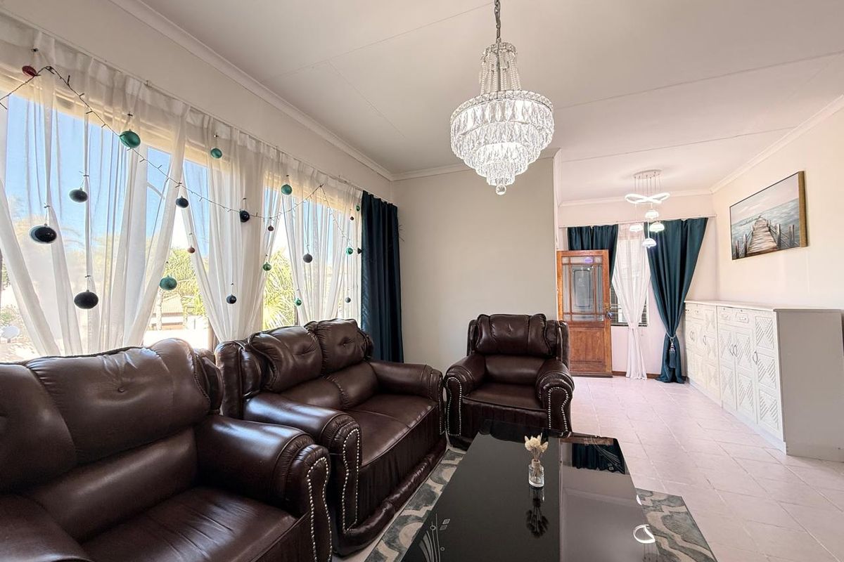 A spacious living room featuring large windows, tiled flooring, a decorative crystal chandelier, and built-in cabinetry, offering a bright and functional living space.