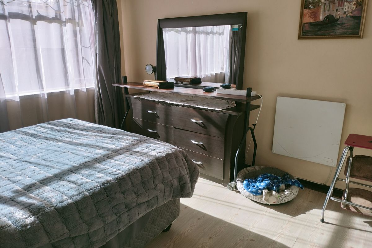 A bedroom featuring light-toned wood-look flooring, a wall-mounted electric heater, and natural light streaming through the window.