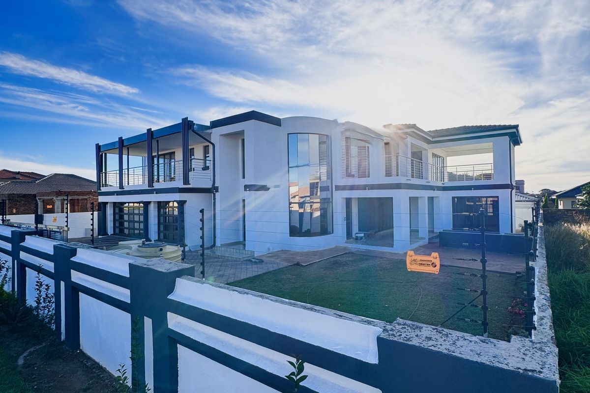 A modern multi-story residential property featuring a large rear garden, paved patio, balconies, and extensive glass facade elements.