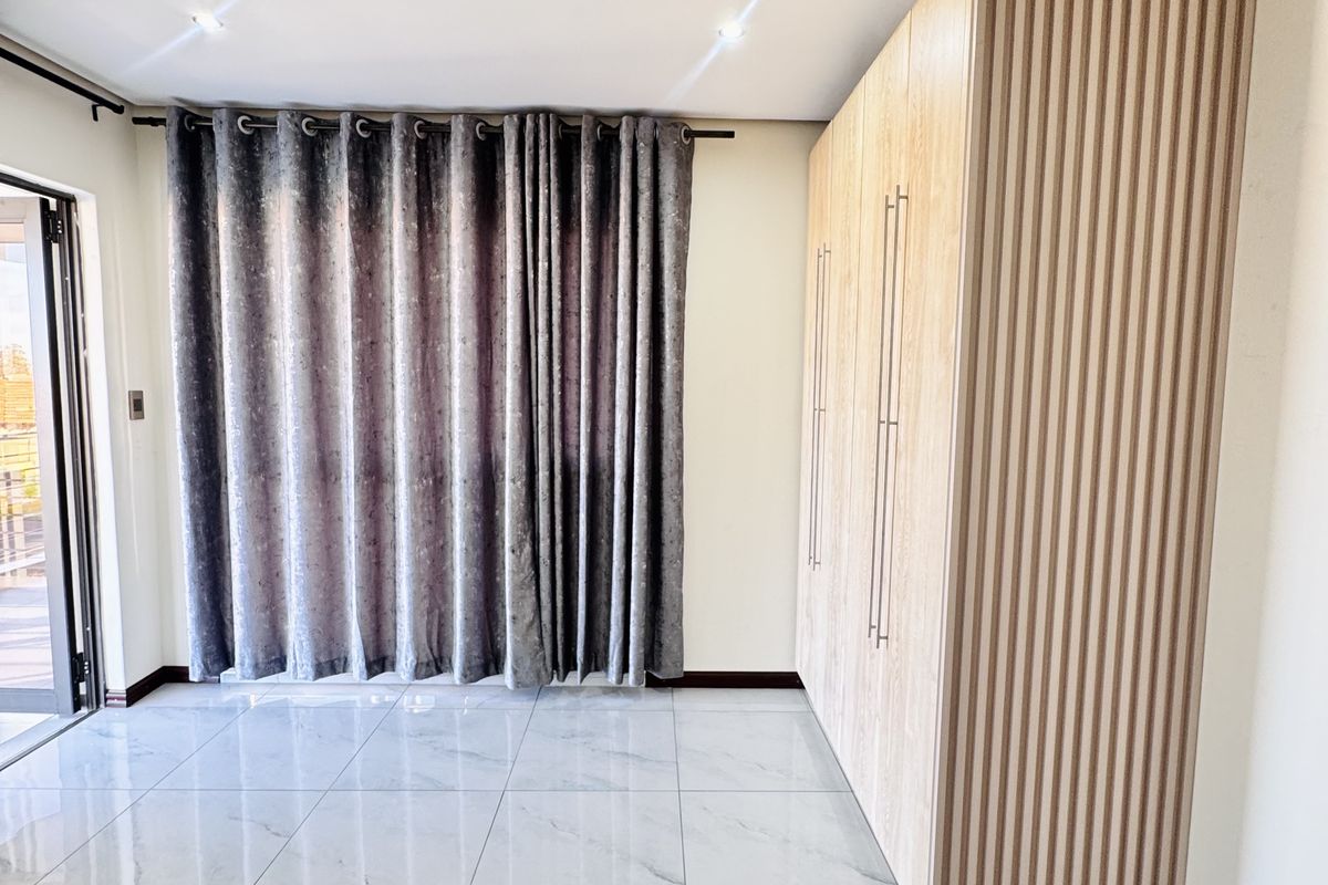 A bright, modern bedroom featuring large-format marble-look floor tiles, a sleek built-in wardrobe with a decorative slatted timber panel, and direct access to a balcony.