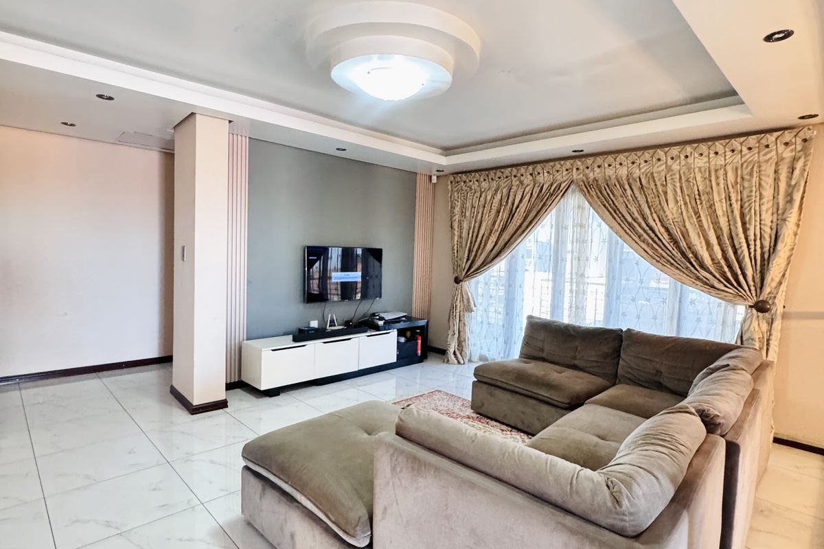 A spacious living room featuring modern tiled flooring, a recessed ceiling with integrated lighting, and a dedicated feature wall for media setup.