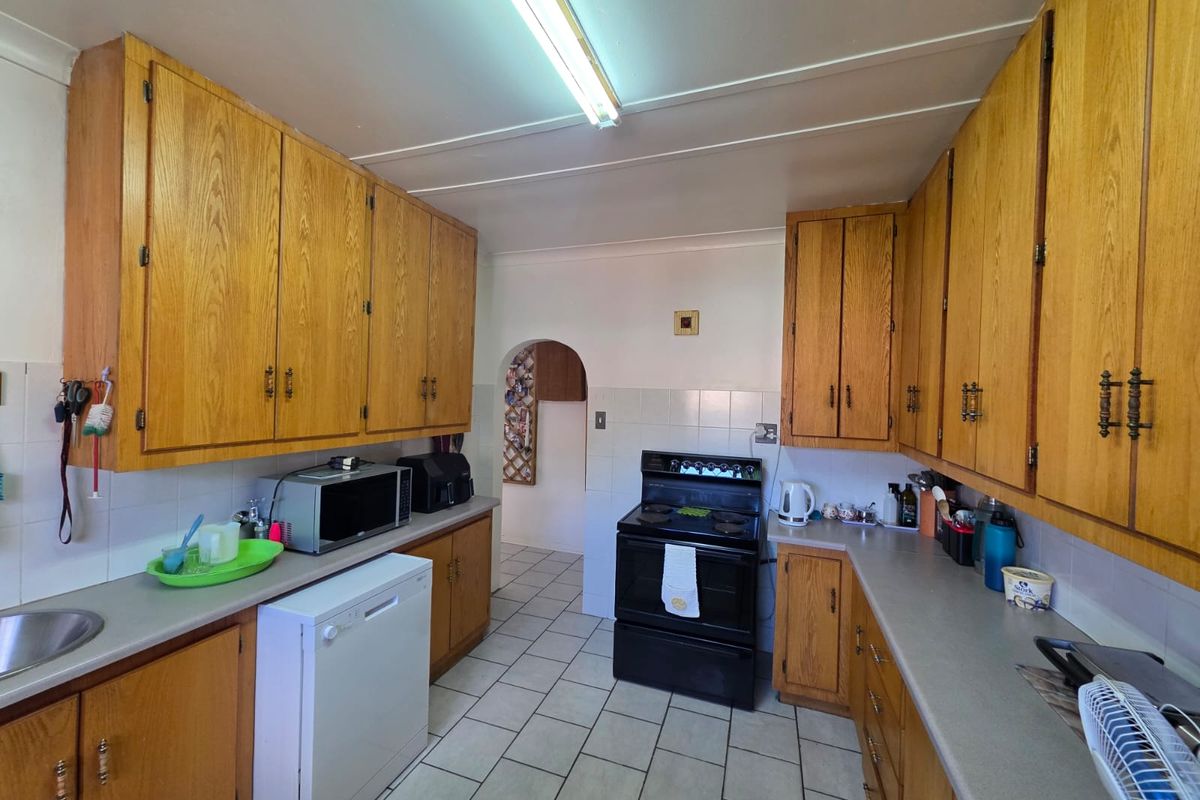 A functional kitchen featuring traditional oak-style cabinetry, tiled splashbacks, and a tiled floor, offering a classic layout with potential for modern updates.