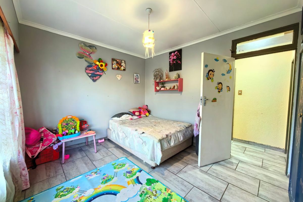 A functional bedroom featuring tiled flooring, a central pendant light fixture, and a standard interior door leading to an adjacent hallway.