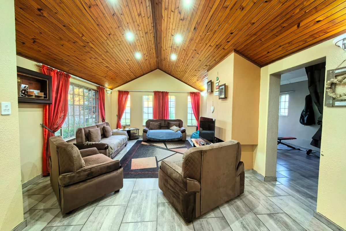 Spacious living room featuring a high vaulted timber ceiling, recessed lighting, and modern tiled flooring with large windows providing natural light.