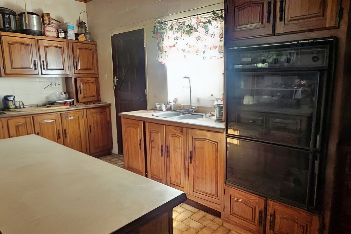 A traditional kitchen featuring extensive wooden cabinetry, a double wall oven, extractor fan, and a central island with tiled flooring.