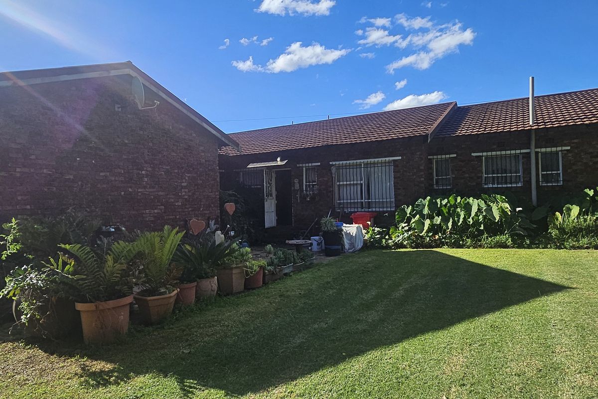 Rear view of the property featuring a brick exterior, tiled roof, attached garage, and a well-maintained lawn area.