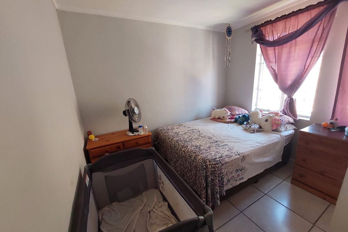 A standard bedroom featuring tiled flooring and a window with security bars, providing a functional living space.
