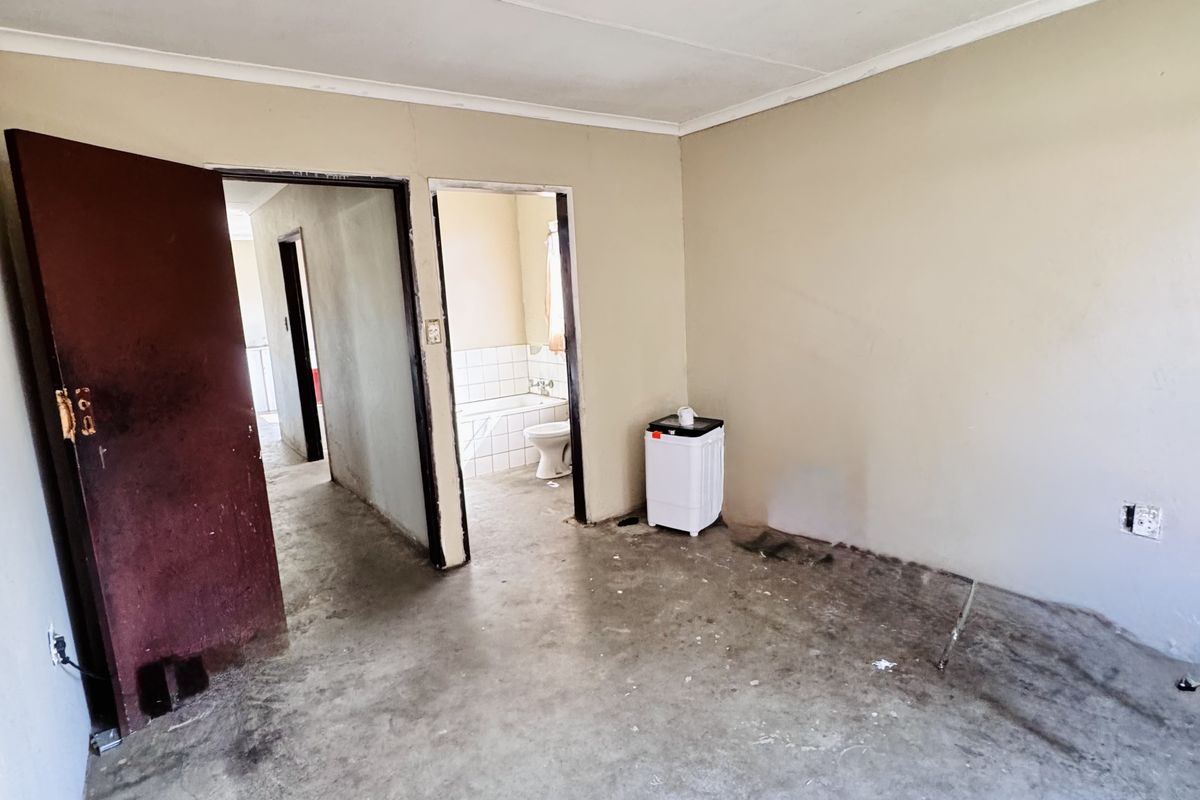 An empty room with exposed concrete flooring and direct access to an adjacent bathroom, requiring significant renovation and cosmetic updates.