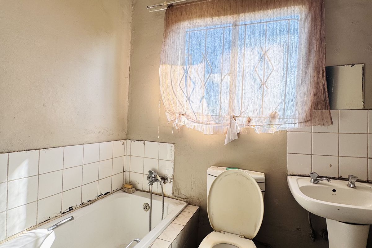A dated bathroom featuring a standard bathtub, pedestal basin, and toilet, requiring significant renovation and cosmetic updates to restore functionality and aesthetic appeal.