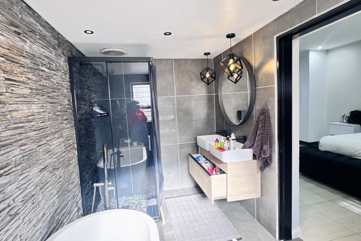Modern bathroom featuring a freestanding bathtub, glass-enclosed shower, floating double vanity, and contemporary stone-cladding feature wall with recessed downlighting.