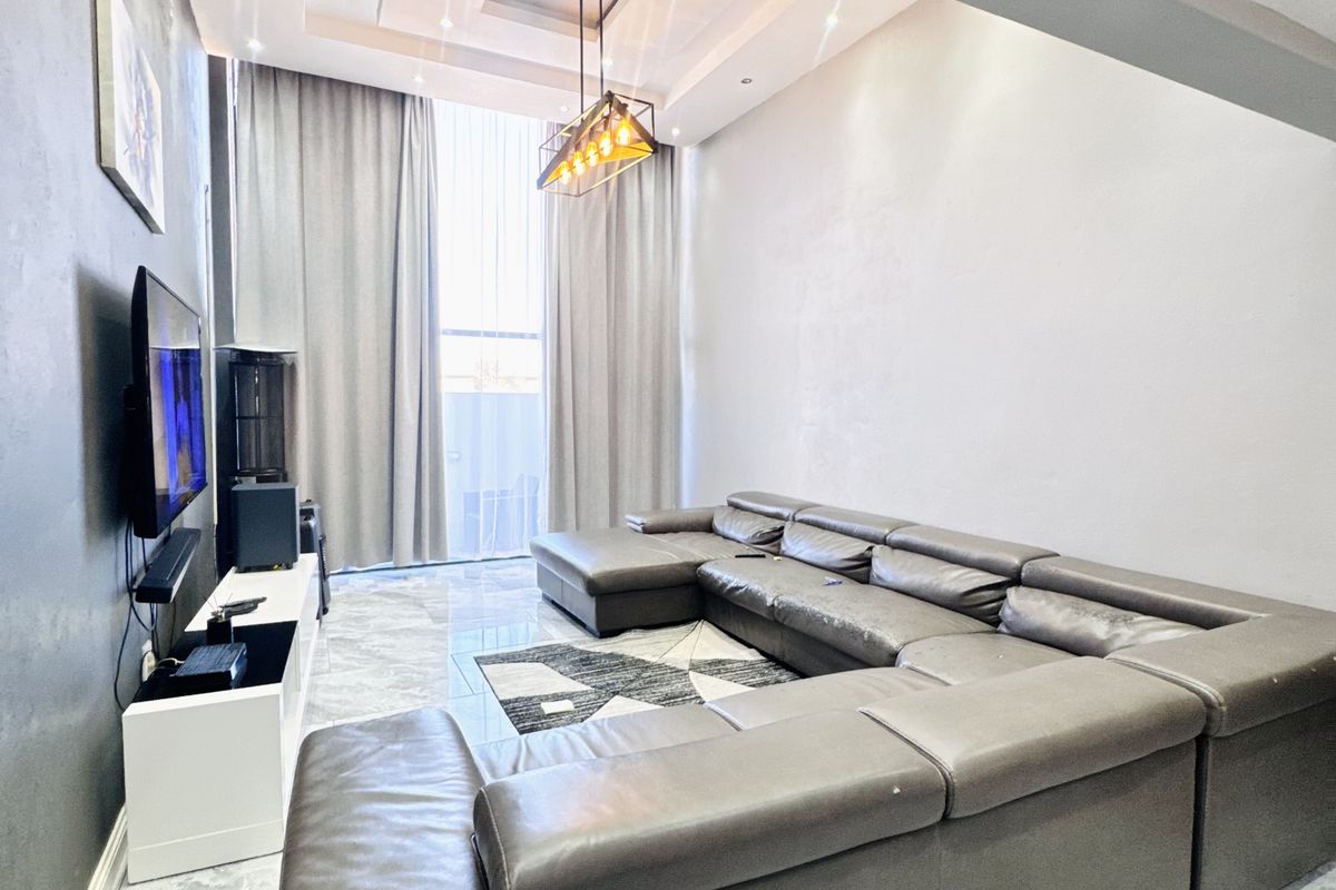 Modern living room featuring high ceilings with recessed tray lighting, large floor-to-ceiling windows, and polished marble-look floor tiles.