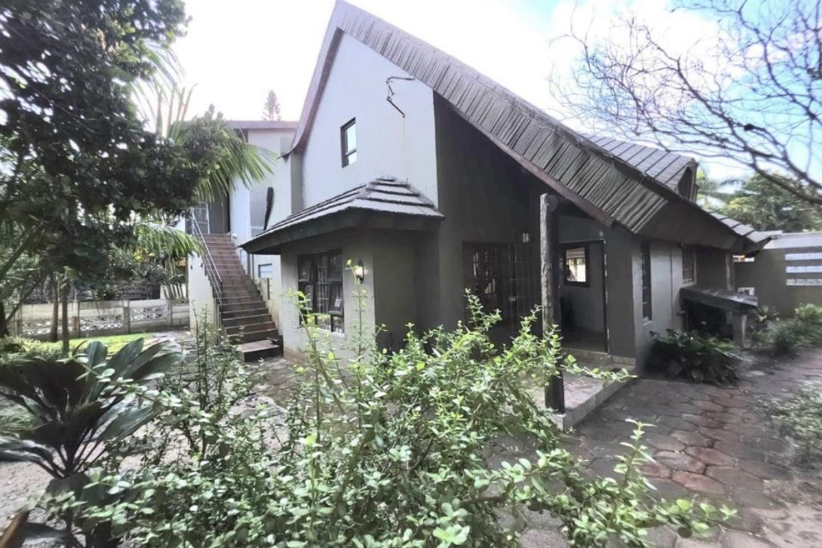 Rear view of the property featuring a paved patio area, external staircase, and a pitched roof design with visible exterior wall finishes.