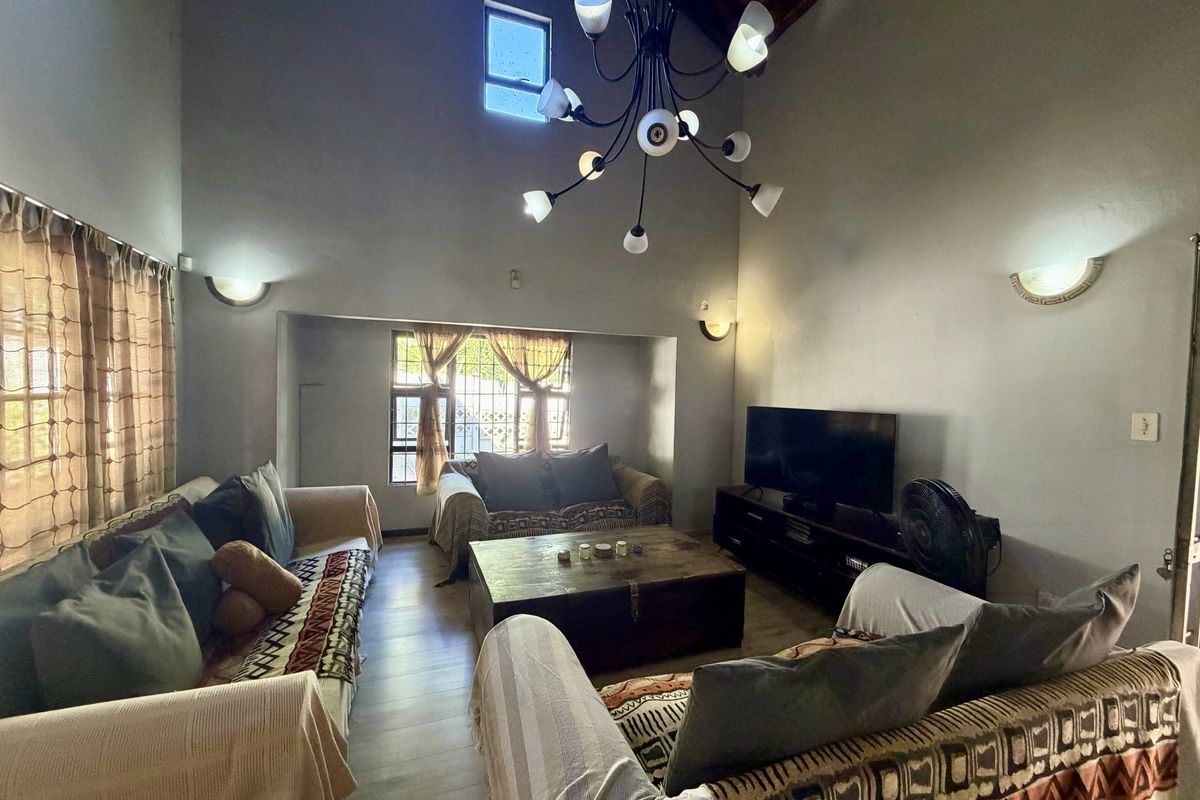 Spacious living room featuring a high vaulted ceiling with exposed timber beams, wall sconce lighting, and large windows with security bars.