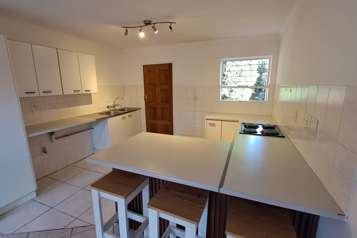Functional kitchen featuring white cabinetry, a built-in electric hob, tiled splashbacks, and a breakfast nook counter, providing a practical workspace for daily meal preparation.
