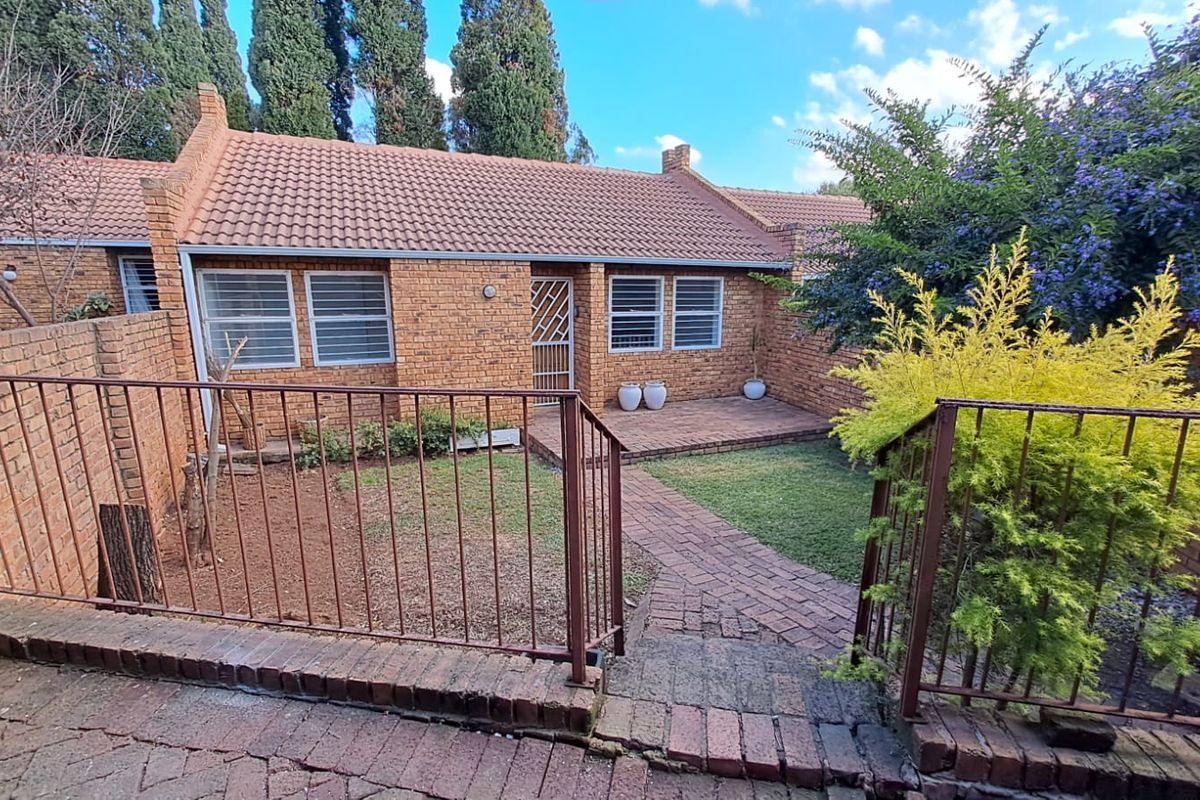 A private rear courtyard featuring a brick-paved patio, small lawn area, and secure metal fencing, providing a low-maintenance outdoor space for the townhouse.