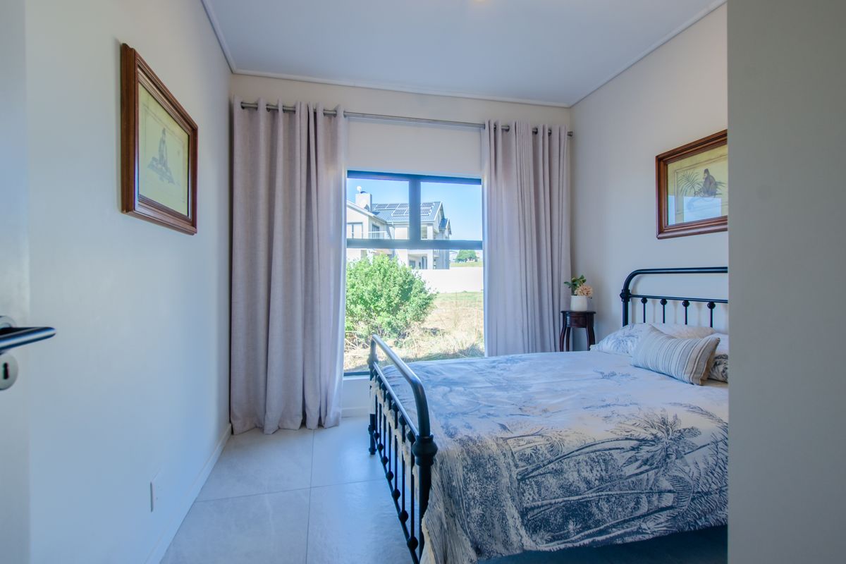 A well-maintained bedroom featuring neutral tiled flooring, a large window providing natural light, and clean, modern finishes.
