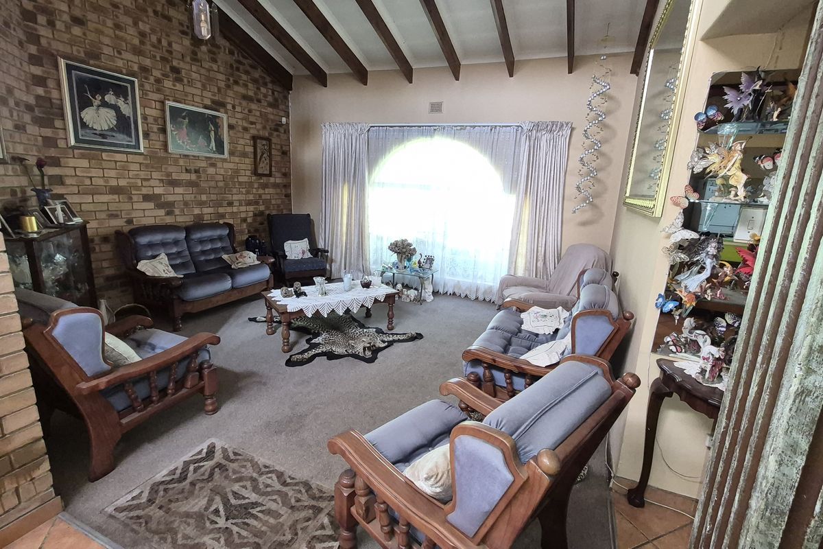 A spacious living room featuring exposed timber ceiling beams, a prominent face-brick feature wall, and a large arched window allowing natural light.