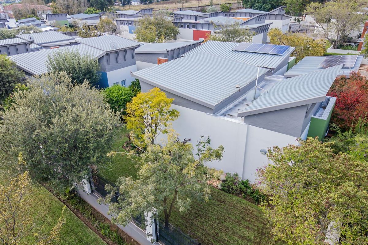 Aerial view of a townhouse complex featuring modern corrugated metal roofs, integrated solar panels, and well-maintained private garden spaces.