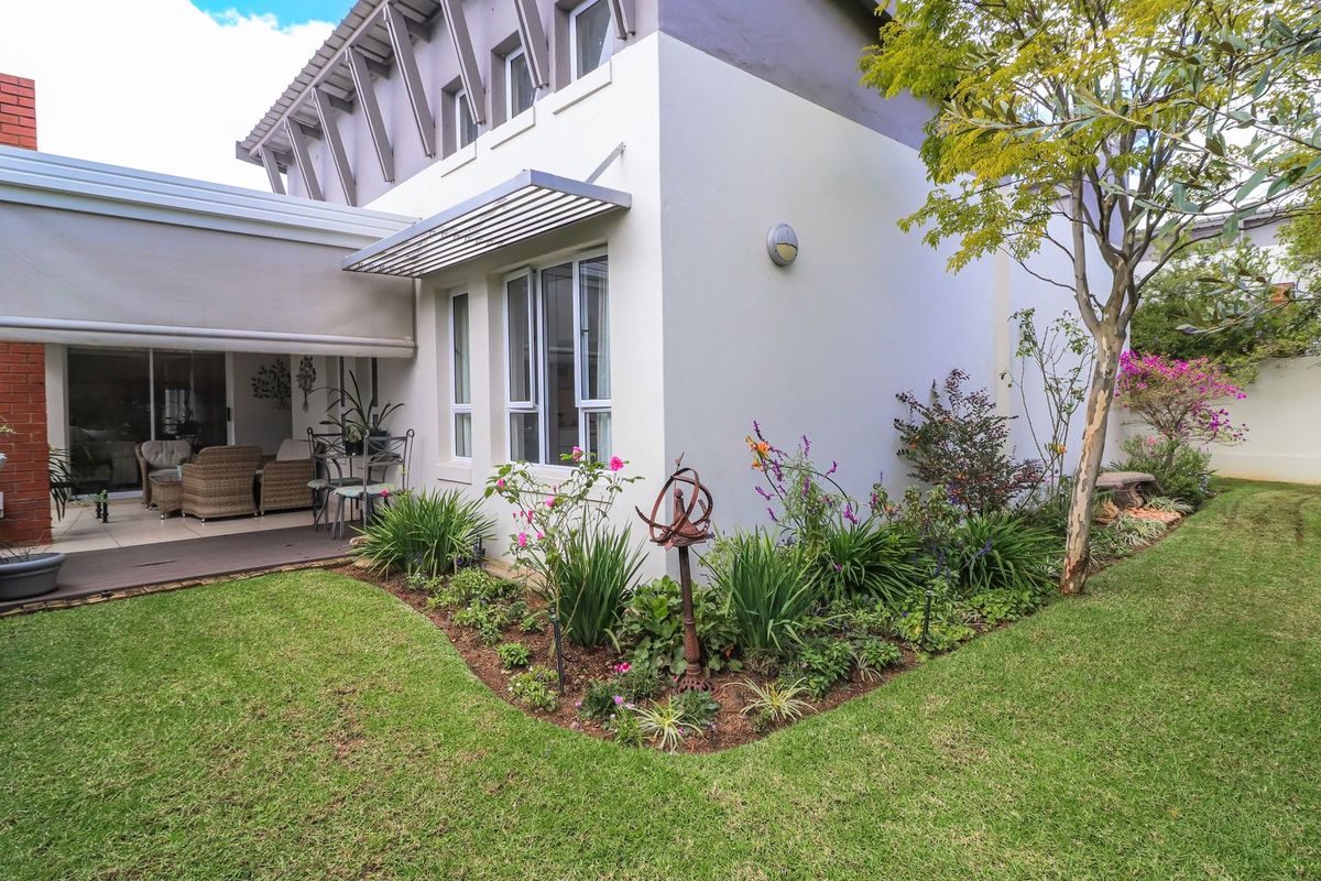 Rear view of the townhouse featuring a well-maintained garden, a covered patio area with a retractable awning, and established landscaping.