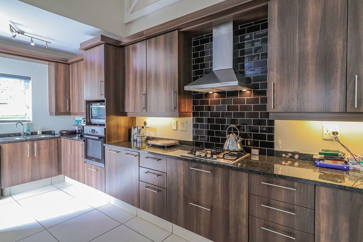 Modern kitchen featuring dark wood cabinetry, granite countertops, a gas hob with extractor fan, and a stylish black subway tile backsplash.