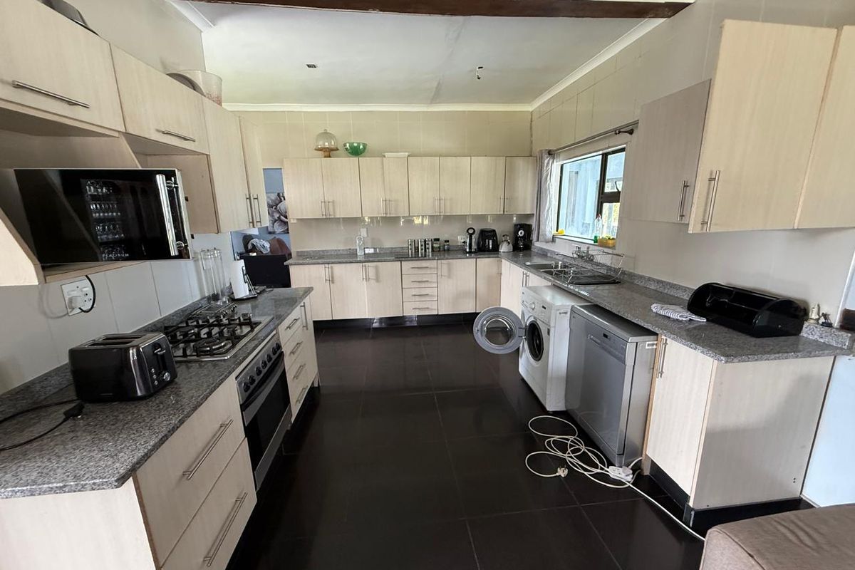 A functional kitchen featuring light-toned cabinetry, granite countertops, a gas hob, built-in oven, and integrated space for laundry appliances.