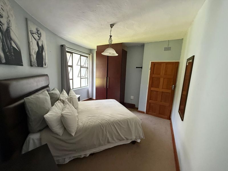 A bedroom featuring a built-in wardrobe, carpeted flooring, and a large window providing natural light.