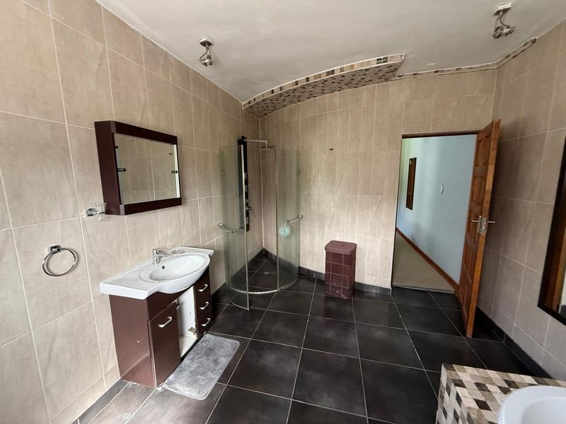 A functional bathroom featuring a corner glass shower enclosure, a wall-mounted vanity with basin, and neutral wall tiling with dark floor tiles.