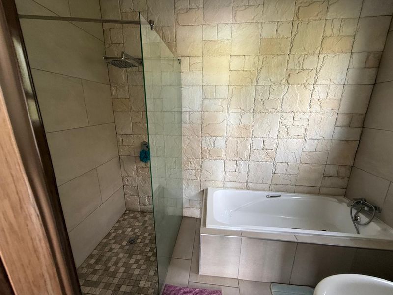 A modern bathroom featuring a walk-in shower with a glass screen, a built-in bathtub, and textured stone-cladding feature walls.