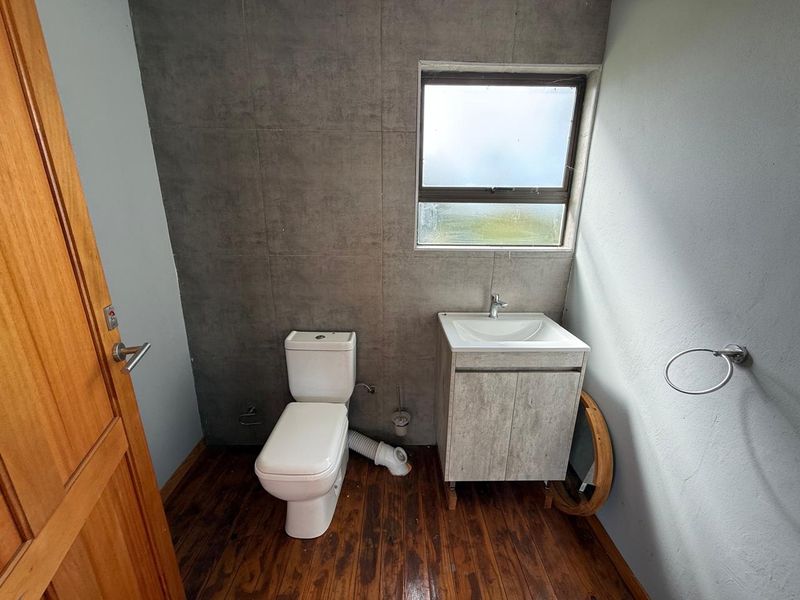 A compact bathroom featuring a modern vanity, toilet, and grey tiled feature wall with timber-look flooring.